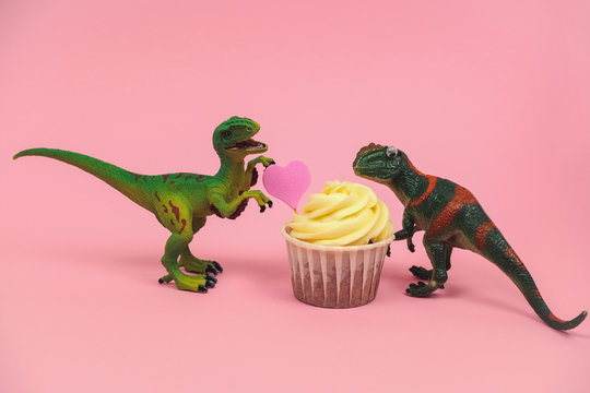 cute green plastic dinosaur toys with cupcakes decorated with pink heart on a pastel pink background