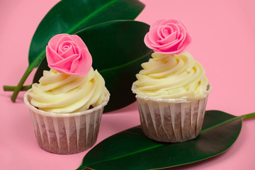 sweet cupcakes decorated with roses and tropical leaves on a pastel pink background selective focus