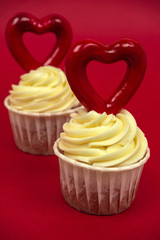 two sweet cupcakes with butter cream decorated with big red heart on a red background