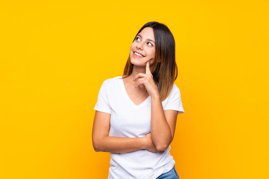 Young woman over isolated yellow background thinking an idea while looking up