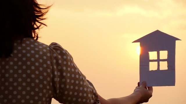 Hand holding a paper house model against the sunset. Happy family concept, construction and real estate transactions.