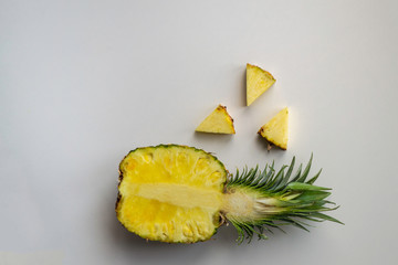 Fototapeta na wymiar .Half a juicy yellow pineapple lies horizontally on a light gray uniform surface. three triangular parts lie side by side. Place for your text.