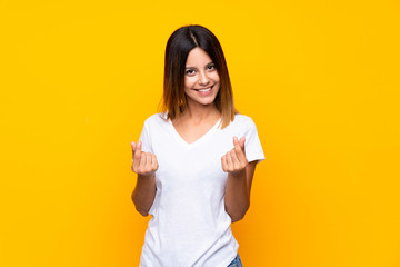 Young woman over isolated yellow background making money gesture