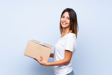 Young woman over isolated blue background holding a box to move it to another site