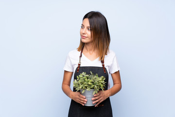 Young woman over isolated blue background taking a flowerpot