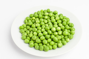 Fresh organic green peas on a white plate isolated on white, side view of healthy raw vegan food, with space for text