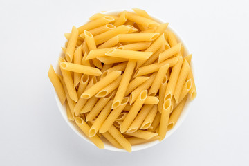 Dried penne Italian pasta in a round bowl ready to be cooked, isolated on white table, top view or flat lay of healthy food