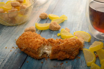 One broken cake, a glass of black tea, pieces of brown sugar and marmalade lemon slices on a wooden background.