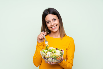 Young woman with salad over isolated green wall