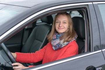 Fototapeta na wymiar young woman in red coat driving black car at city street