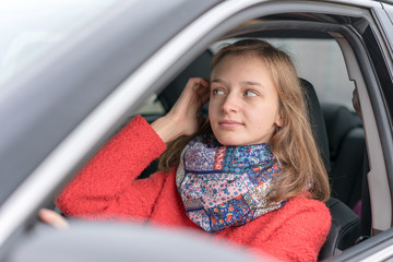 Fototapeta na wymiar woman in red coat driving black car looks in mirror straightening her hairstyles