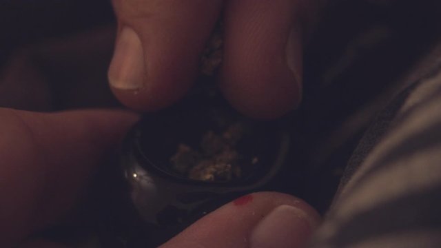 Grinding weed to prepare the glass pipe to smoke cannabis - close up - slow motion