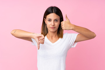 Young woman over isolated pink background making good-bad sign. Undecided between yes or not