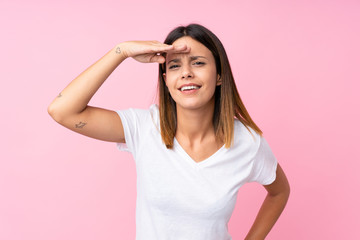 Young woman over isolated pink background looking far away with hand to look something