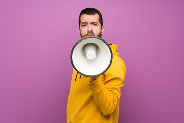 Handsome man with yellow sweatshirt shouting through a megaphone