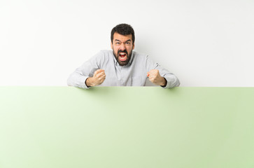 Young handsome man with beard holding a big green empty placard frustrated by a bad situation