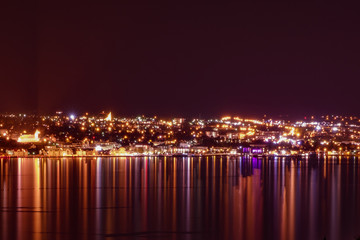 Akureyri at night, in the foreground mirroring water with the lights of the city reflecting in the water