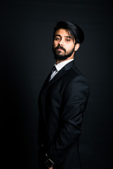 Portrait of a young handsome successful Indian in a classic black three-piece business suit on a dark background