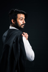 Portrait of a young handsome successful Indian in a classic black three-piece business suit on a dark background, Holding his jacket over his shoulder