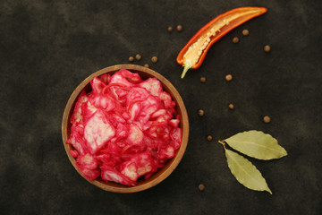 Tasty red sauerkraut or fermented cabbage in marinade in a wooden bowl with spices for decoration on a black background. Fermented food. Korean cuisine. Flat lay. Top view.