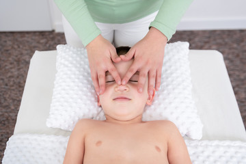 Obraz na płótnie Canvas Kids massage concept background. Female therapist giving a young boy face massage. Top view.