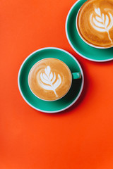 Cyan cappuccino coffee cups over orange background. Top view flat lay with copy space