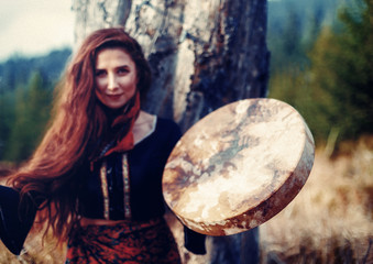 beautiful shamanic girl playing on shaman frame drum in the nature.
