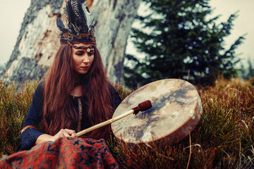 beautiful shamanic girl playing on shaman frame drum in the nature.