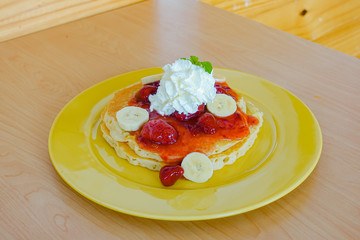 Pancakes served with banana, strawberry, strawberry jam and whipped cream