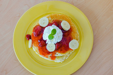 Pancakes served with banana, strawberry, strawberry jam and whipped cream