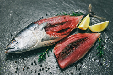 Fresh fish fillet sliced for steak or salad with herbs spices rosemary and lemon - Raw fish seafood on black plate background , Longtail tuna , Eastern little tuna fillet ingredients for cooking food