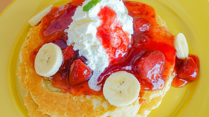 Pancakes served with banana, strawberry, strawberry jam and whipped cream