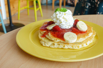 Pancakes served with banana, strawberry, strawberry jam and whipped cream