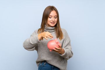 Teenager girl with sweater over isolated blue background holding a big piggybank