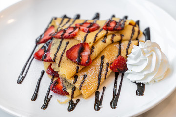 Side view of Strawberry crepe topped with chocolate sauce and whipped cream.