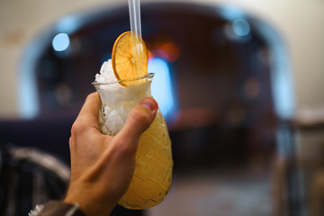 Obraz premium Man hand holding an orange summer cocktail in a medieval restaurant hall - Blurry 1.4 bokeh