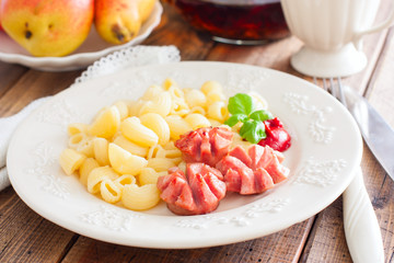 Fried sausages with pasta on a wooden plate on a wooden table, selective focus