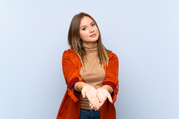 Teenager girl with coat over isolated blue background holding copyspace imaginary on the palm to...