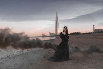 beautiful girl with smoke in hand and in a black dress stands on the shore of the Gulf of Finland...