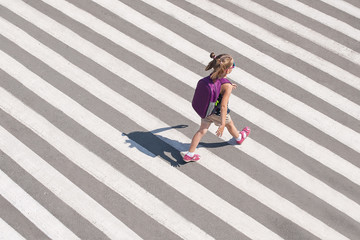 Schoolgirl crossing road on way to school. Zebra traffic walk way in the city. Concept pedestrians...
