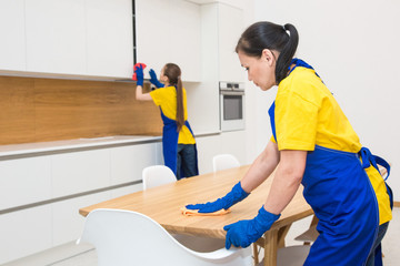 professional cleaning service. Two women in working uniform, in aprons, divide the cleaning of the kitchen of a private house, cottage. washing the refrigerator, tap, sink. Wash floor.