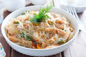 Funchosa with vegetables and chicken on a white plate on a wooden table, selective focus