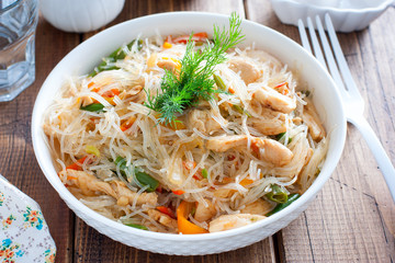 Funchosa with vegetables and chicken on a white plate on a wooden table, selective focus