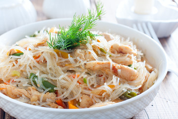 Funchosa with vegetables and chicken on a white plate on a wooden table, selective focus