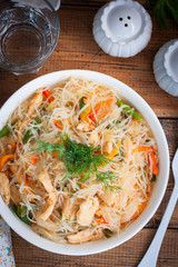 Funchosa with vegetables and chicken on a white plate on a wooden table, selective focus