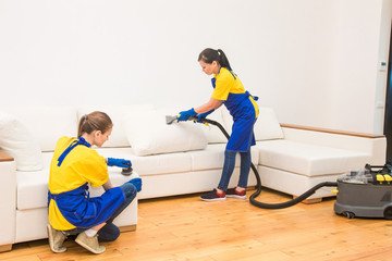 professional cleaning service. Two women in working uniform, in aprons. Two women in working uniform, in aprons, divide the cleaning of private house, cottage. Washing , vacuum cleaning the sofa