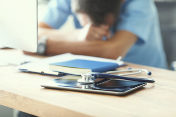 Tired man doctor sleeps lying on his hands while sitting at a computer desk. Doctor works on a computer in the clinic after a night shift.