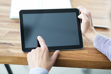Man's hands holding blank tablet device over a wooden work space table.