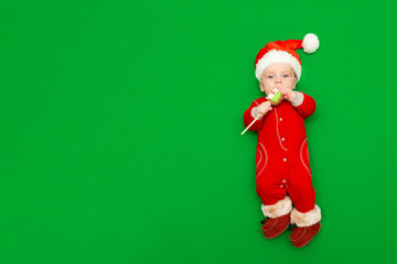 A newborn boy in a red Santa suit, fur boots and a Christmas hat with a Christmas gingerbread in his hands on a green screen. The view from the top. Space for text. Layout for designers