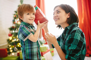 Happy family mom and son on a Christmas winter sunny morning in a decorated Christmas celebration room with a Xmas tree and gifts.